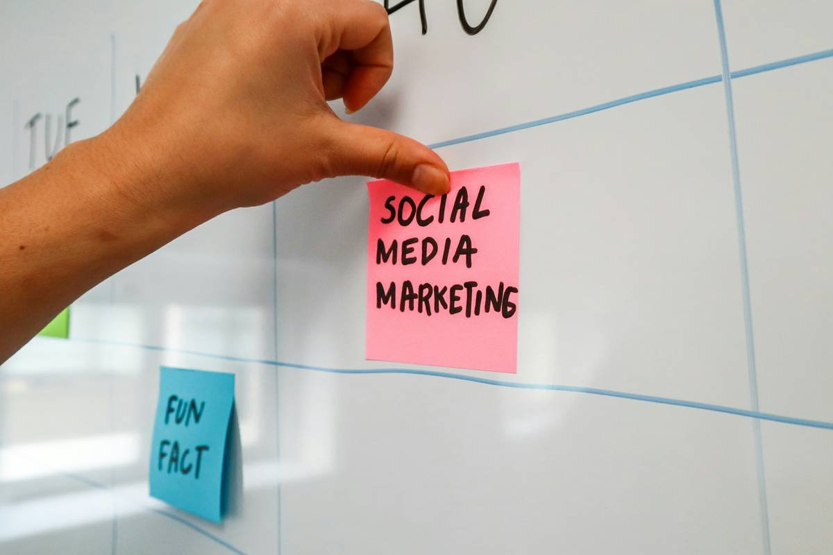Person sticking a post-it on a white board with the words "Social Media Marketing" written on it