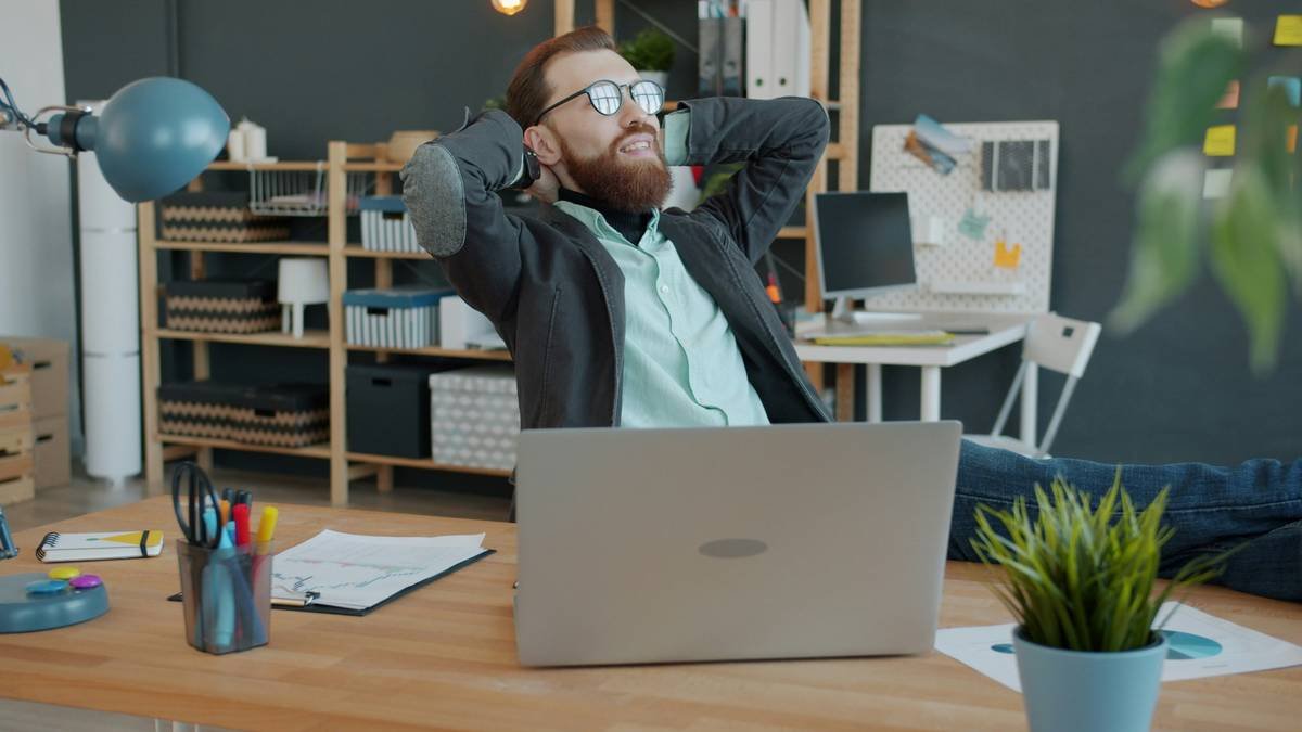 Portrait of happy guy relaxing in office sitting at desk smiling enjoying break and dreaming. Suceessful people, youth and creative workplace concept.